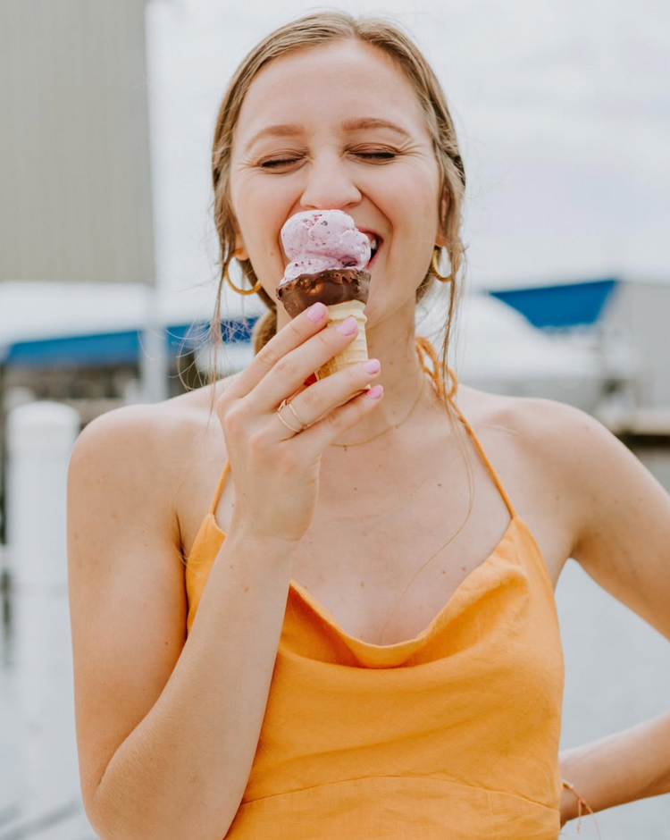 Woman in an orange dress eating Aruba Freeze Nitrogen ice cream cone outdoors.